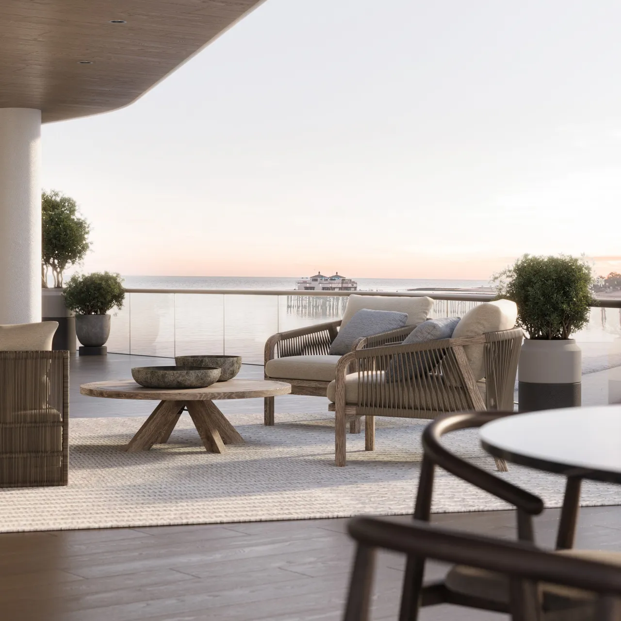 Modern oceanfront balcony featuring rope-accented lounge chairs, natural wood coffee table, and panoramic views of a serene sunset over the water.